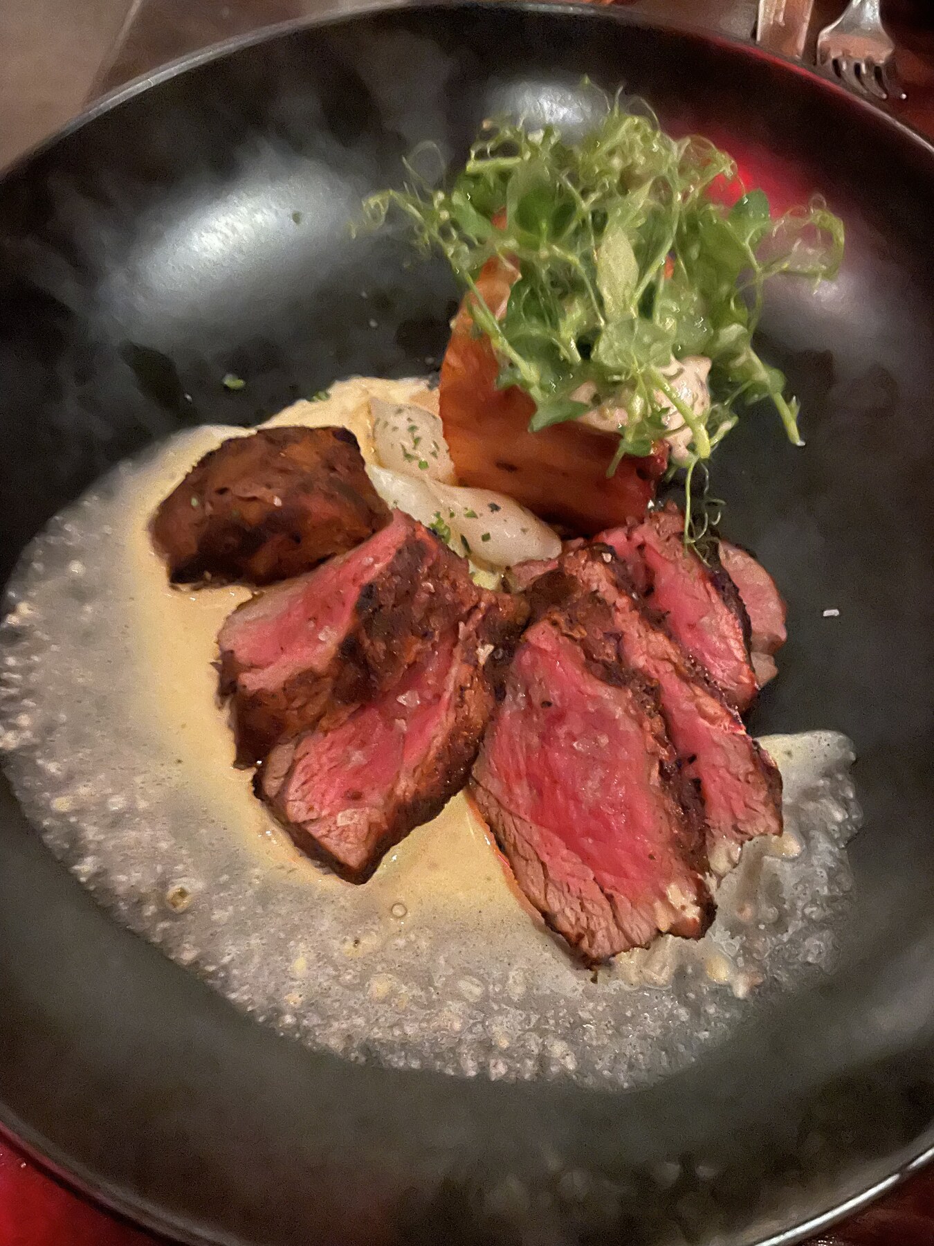 Sliced steak plated with greens and a golden sauce